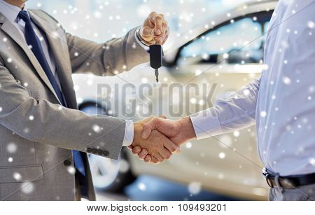 auto business, car sale, deal, gesture and people concept - close up of dealer giving key to new owner and shaking hands in auto show or salon over snow effect