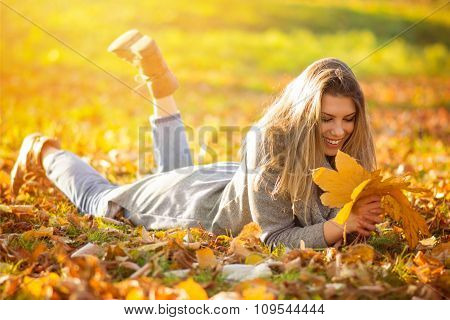 Happy young woman with leaves in park in autumn