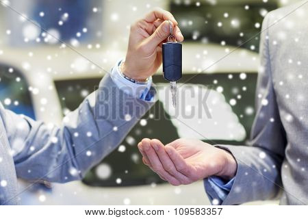 auto business, car sale, deal and people concept - close up of male hands with car key in auto show or salon over snow effect