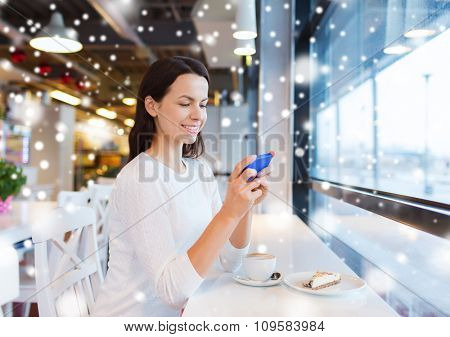 drinks, food, people, technology and lifestyle concept - smiling young woman with smartphone drinking coffee at cafe over snow effect