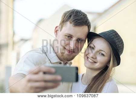 Touristic couple shooting on the modile phone selfy at the city streets under sunlight.