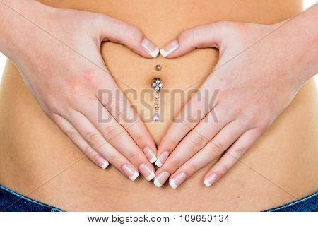 a woman has abdominal pain or stomach pain. hands in heart shape around navel piercing.