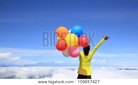 young woman with balloons on mountain peak