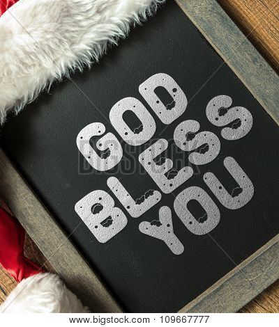 God Bless You written on blackboard with santa hat