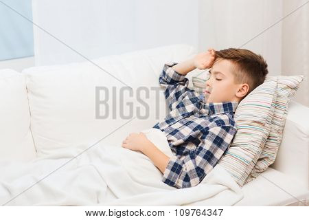 childhood, healthcare, people and medicine concept - ill boy with flu lying in bed at home and suffering from headache