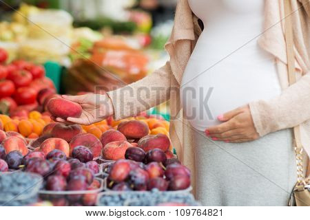 sale, shopping, pregnancy and people concept - close up of pregnant woman choosing saturn peaches at street food market