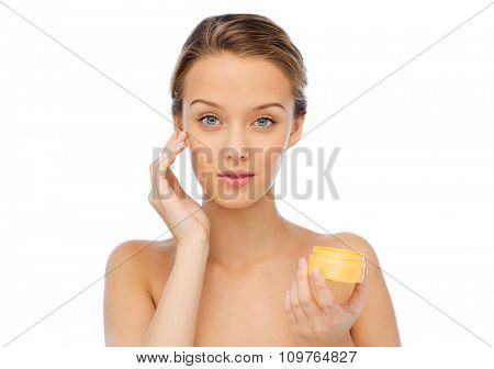 beauty, people, cosmetics, skincare and cosmetics concept - young woman appying cream to her face
