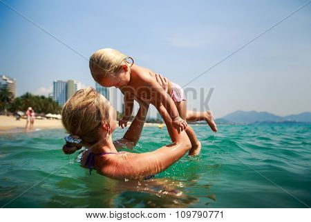 Side-view Mother In Sea Laughs Holds In Arms Small Daughter