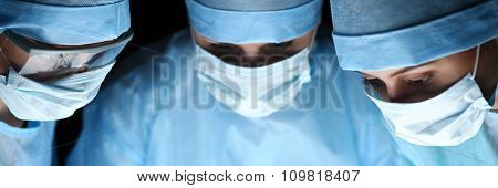 Three Surgeons At Work Operating In Surgical Theatre