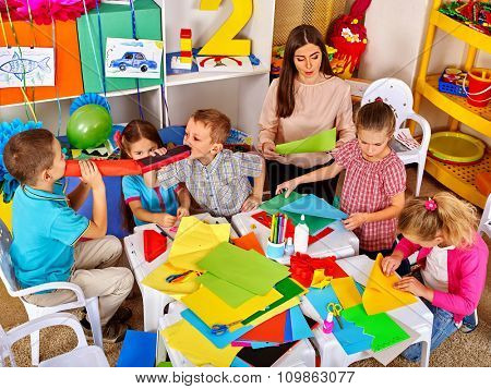 Kids with young teacher woman painting on paper at table  in  kindergarten . Top view.