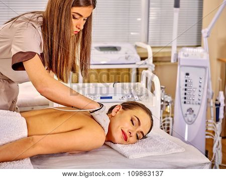 Woman  receiving electric back massage at beauty salon. Beautician wearing electricity gloves. In room is device for hardware cosmetology. 