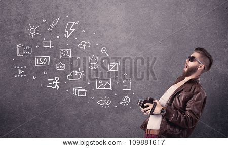 An elegant hipster guy trying to use a vintage camera with camera settings icons drawn on wall, like flash, white balace or ISO value concept