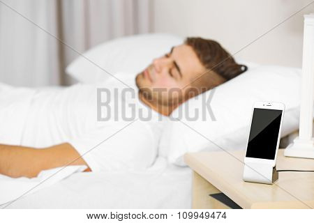 Beautiful young man waking up with mobile alarm clock