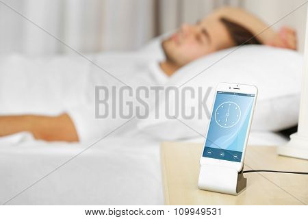 Beautiful young man waking up with mobile alarm clock