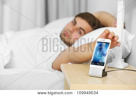 Beautiful young man waking up with mobile alarm clock