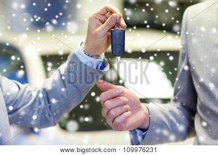 auto business, car sale, deal and people concept - close up of male hands with car key in auto show or salon over snow effect