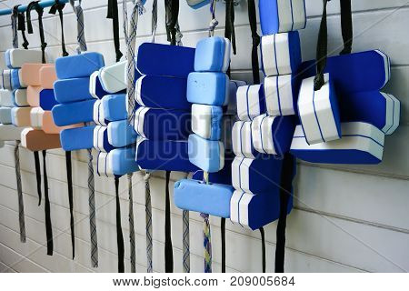 A Row Of Swimming Belts Hanging On Pvc Bar By Swimming Pool Against White Pattern Wall.