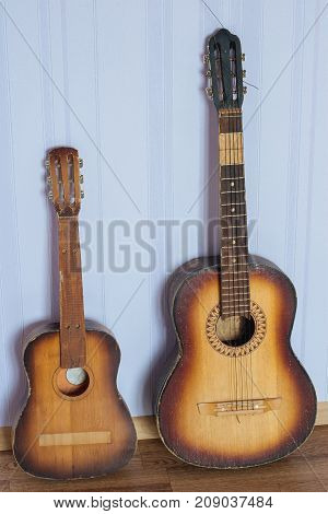 Two old broken guitars of a different size standing by the wall on the floor in the room: one is a regular one and another  is a child.