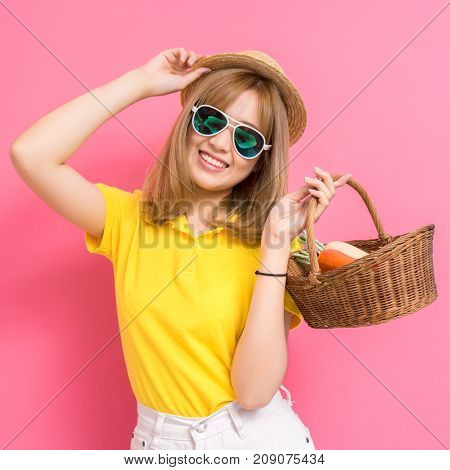 Fashion portrait of girl shopping concet. young beautiful asian with relax dress yellow shirt and white jeans pants hat sunglasses basket vegetables in summer lifestyle on pink background.