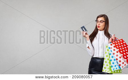 The brunette woman in a shirt and skirt with credit cart  and packeges in hands on a gray background. Place for text.