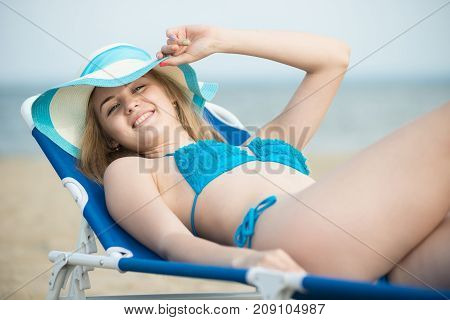 Young lady sunbathing on a beach. Beautiful woman posing at the summer sand beach. Outdoor summer portrait of pretty sport style woman in blue bikini. Ocean sea coast. Beautiful fit tan girl. Sexy slim model caucasian ethnicity outdoors.