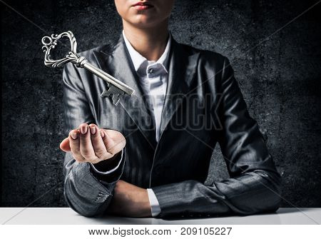 Cropped image of businessman in suit keeping big key in hand with dark wall on background.