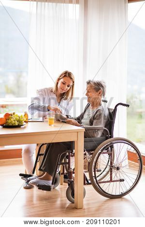Health visitor and a senior woman with tablet during home visit. A nurse talking to an elderly woman.