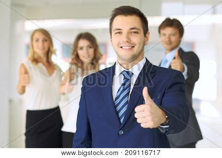 Successful young business people showing thumbs up sign while standing in office interier