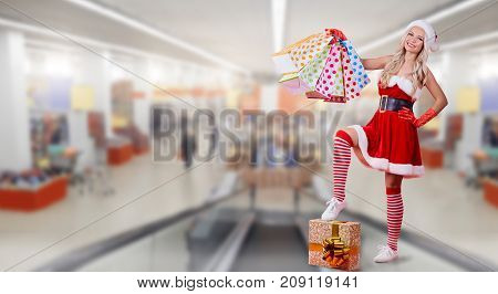 A girl in Santa Claus costume with a package of gifts on the background of the trading center.