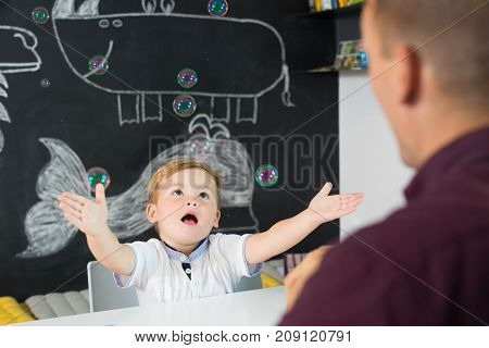 Cute little playfull toddler boy amazed by milky bubbles at child therapy session. Private one on one homeschooling with didactic aids.