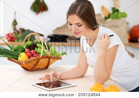 Young woman is making online shopping by tablet computer and credit card. Housewife found new recipe for cooking in a kitchen.