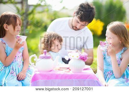 Father playing tea party with his three adorable daughters. Having many children single father. Loving and caring father. Single parent. Beautiful decorated tea party outdoors at the backyard. male babysitter sitter childminder sitter-in.
