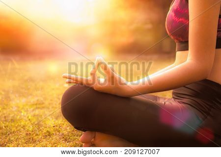 Healthy woman doing Yoga meditation on green lawn with sunset morning in plublic park Singapore.