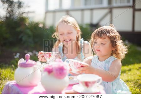 Adorable little sisters dressed like princesses playing tea party. Beautiful decorated tea party outdoors at the backyard.
