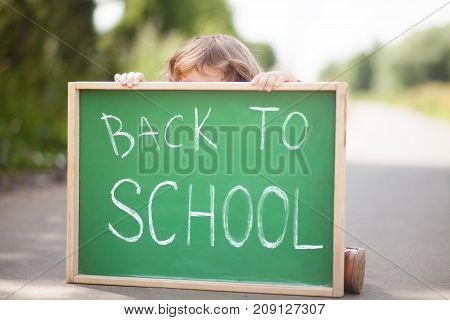 Adorable little girl hiding behind the chalkboard don't want back to school. Have promlems with schoolmates or teathers. Stressed outsider kid. Teathers pressure consept. Negative feelings fear of school.