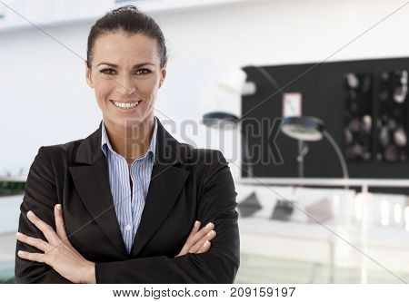 Trusty female business professional smiling, standing arms crossed in modern office lobby.