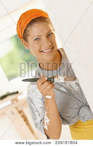 Woman renewing home. Happy young woman painting wall with paint brush in her fixer upper, smiling.