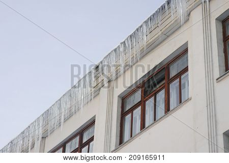Large icicles hang on a house roof. Winter cityscape