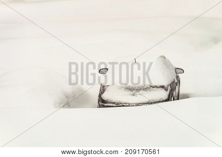 Snow-covered car left amidst large snowdrifts. Bad snowy winter weather. Car blocked after heavy snowstorm.