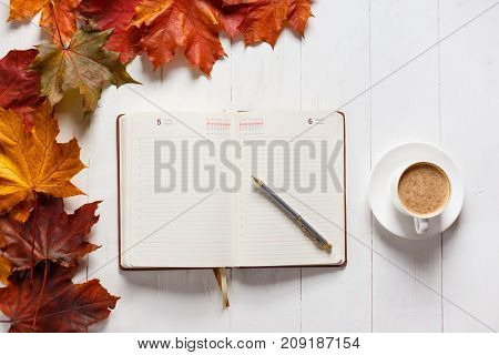 The concept of autumn mood. Morning coffee, diary and colored maple leaves. Top view.