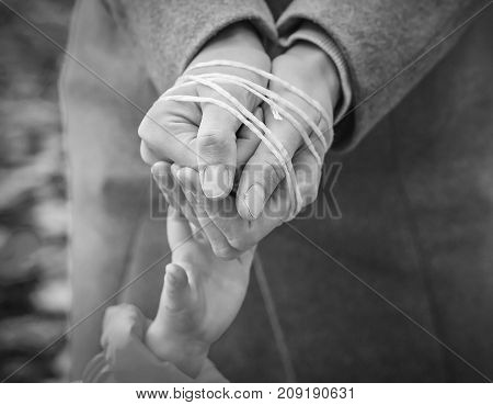 child's hand reaches out to the rope-tied hands of the parent. Black and white image. Woman's hands tied with rope. Violence in family concept