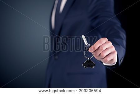 Young businessman hand over keys with empty dark background