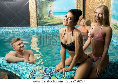 Two young pretty girls in bicini spending time with their boy friends in a luxurious swimming pool in sauna