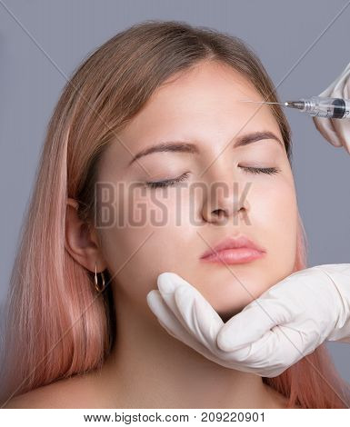 Beautiful young woman with red lips gets cosmetic injection, isolated over greye background. Doctor is making an injection in face. Beauty Treatment.
