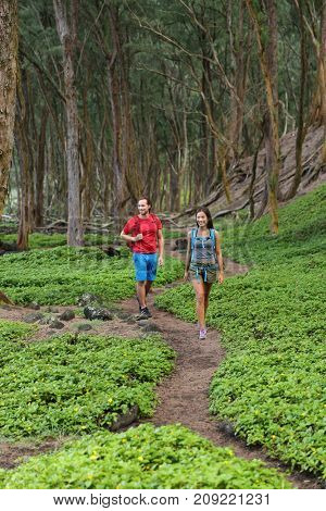 Outdoor nature people walking in forest hiking on trail path in Hawaii mountains rainforest. Happy couple with backpacks going camping with bags, enjoying landscape. Tourists on tropical travel.
