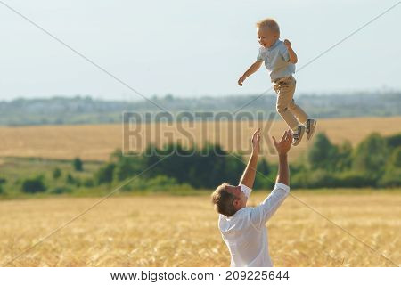 Father playing with son on summer weadow. Family walking with child outdoor