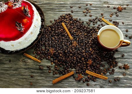 A cup of coffee with a big cake and coffee beans, anise and cinnamon on a wooden table. view from above
