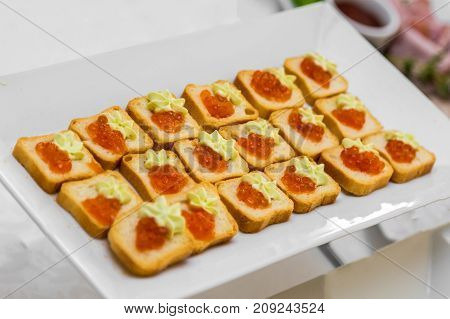 Bread with caviar on a white plate of the banquet table.