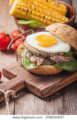 Homemmade Bacon Hamburger with fried Egg, Lettuce and lentil burger with a garnish of corn and tomatoes