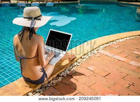 Women wearing bigini or swimware suits swimming pool using laptop computer at the resort town of Pattaya in Thailand.